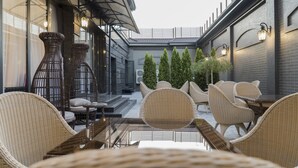 Un espace extérieur aménagé avec des meubles en osier et une table en verre, entouré d’un mur de briques et de verdure.