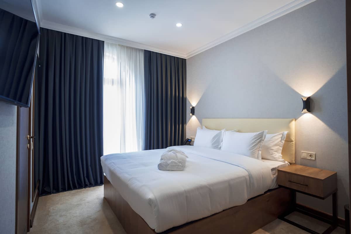 Una habitación de hotel con una cama grande, una mesita de noche y una lámpara fijada a la pared.