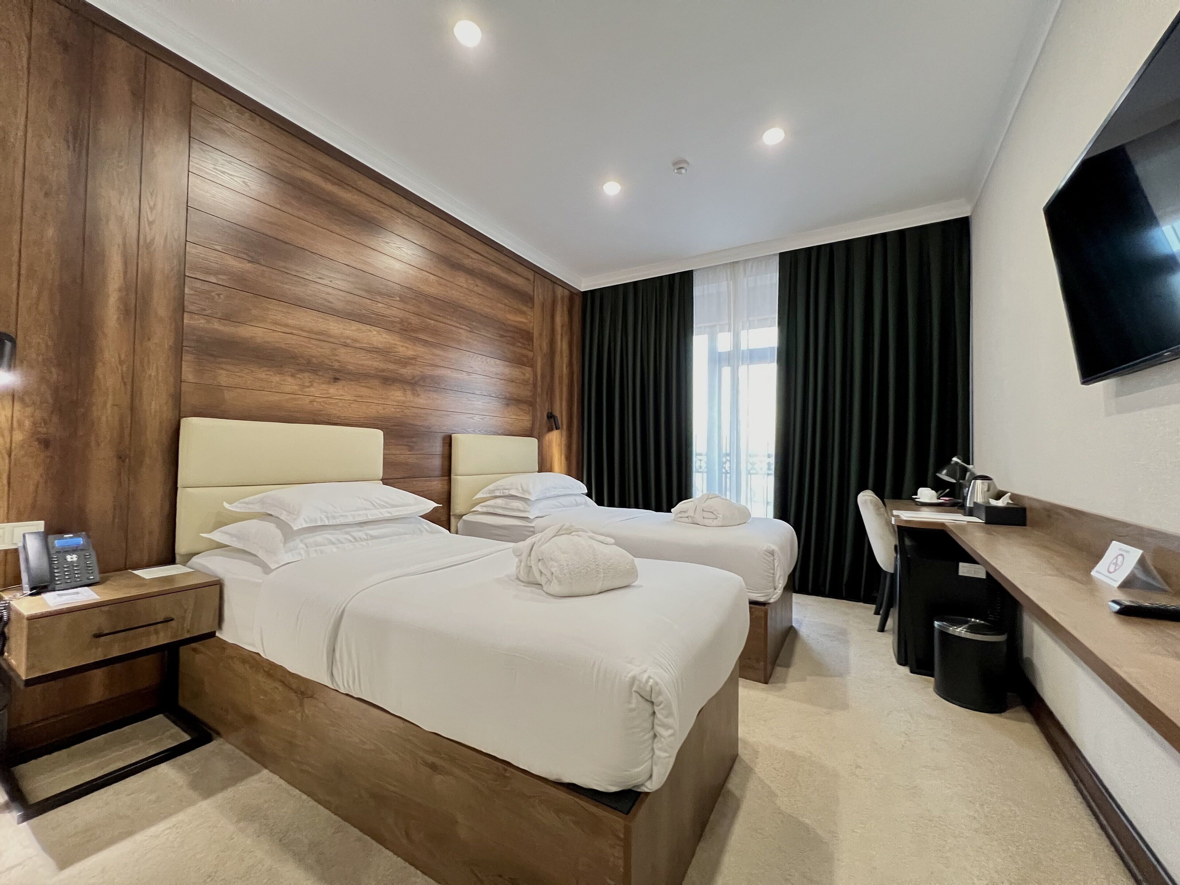 A hotel room with two beds, a desk, a chair, a TV, and a telephone on the nightstand.