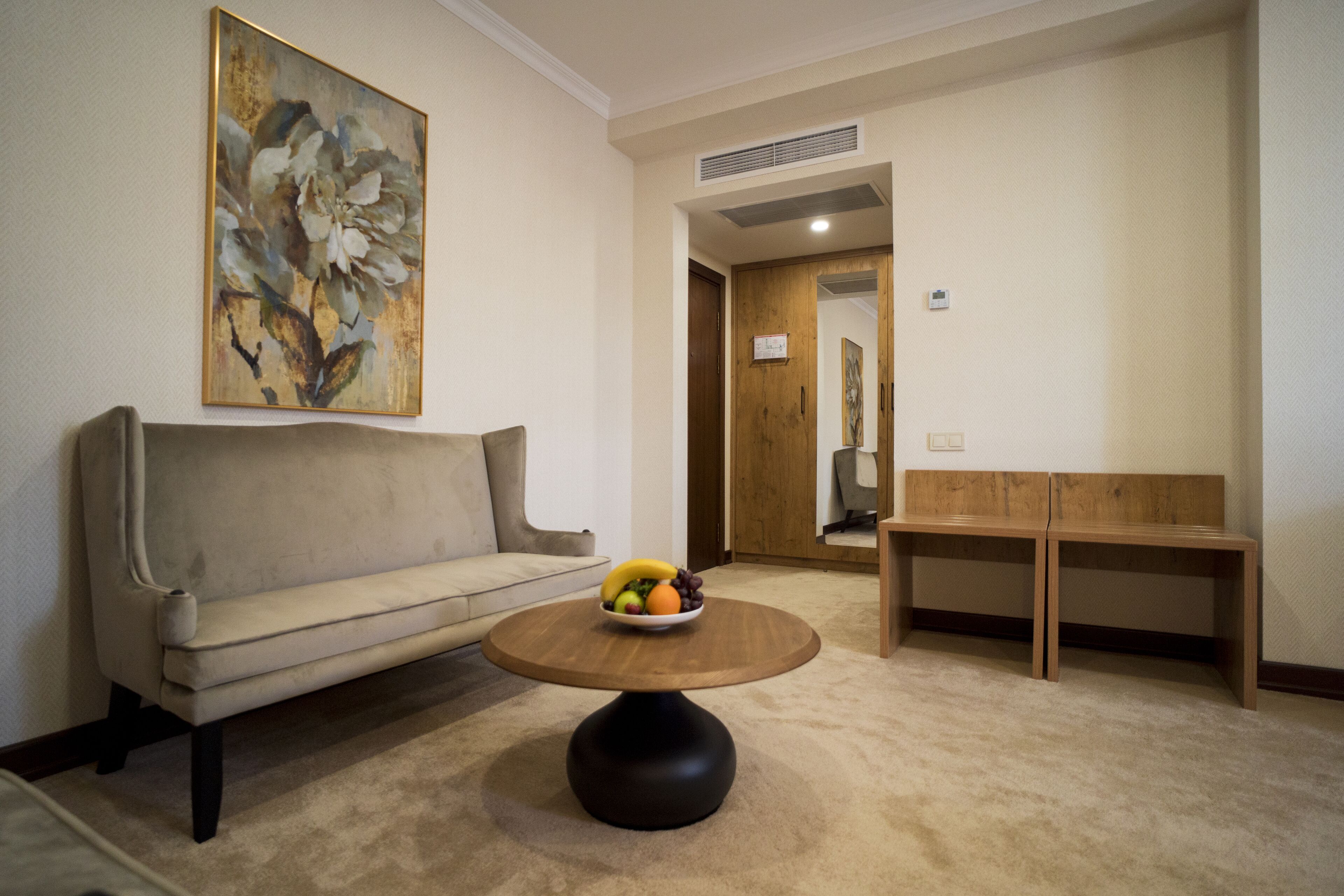 Una sala de estar con un sofá, una mesa redonda de madera con fruta y un cuadro en la pared.