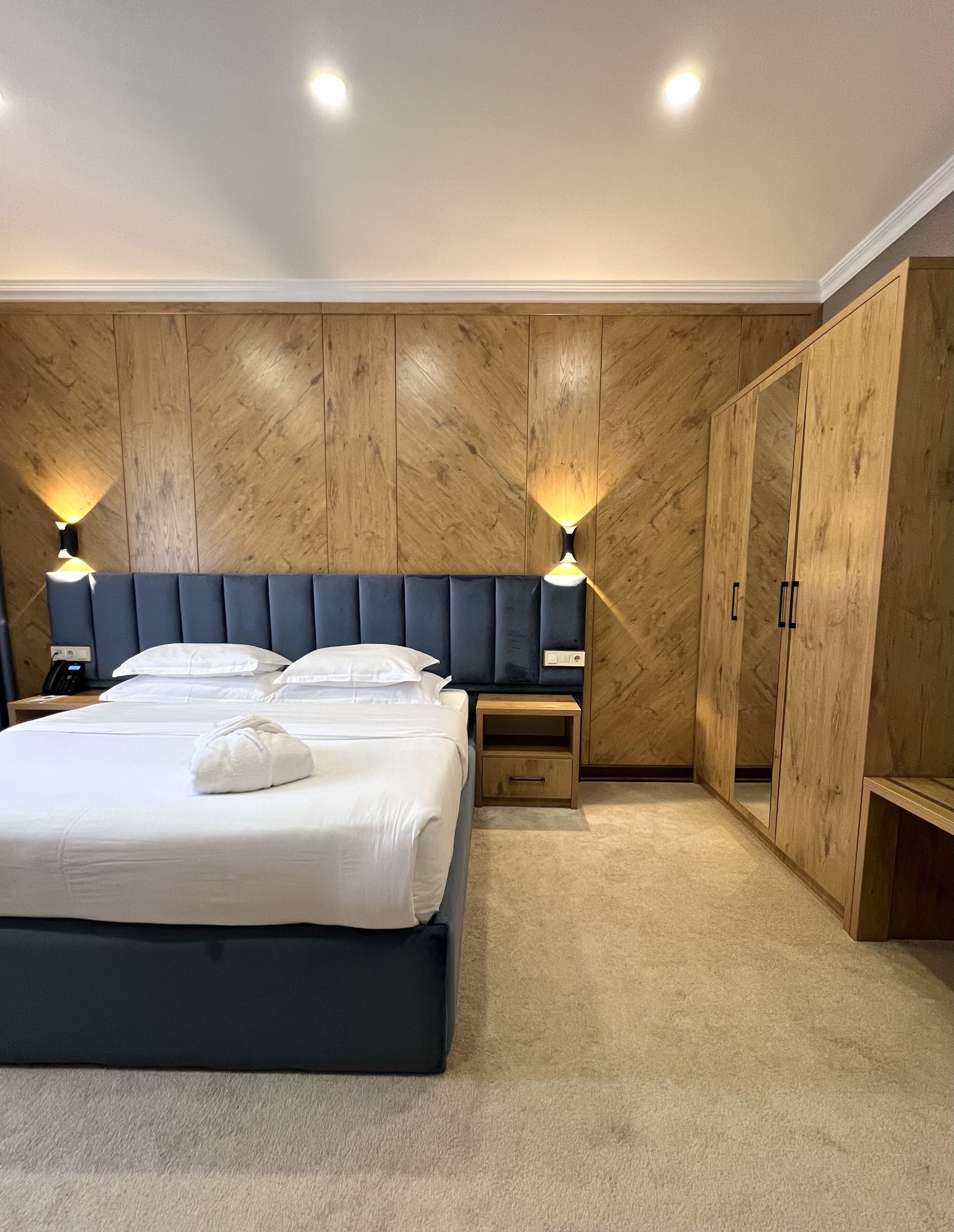 Un dormitorio con una cama grande, dos mesitas de noche, un armario y paredes de paneles de madera.
