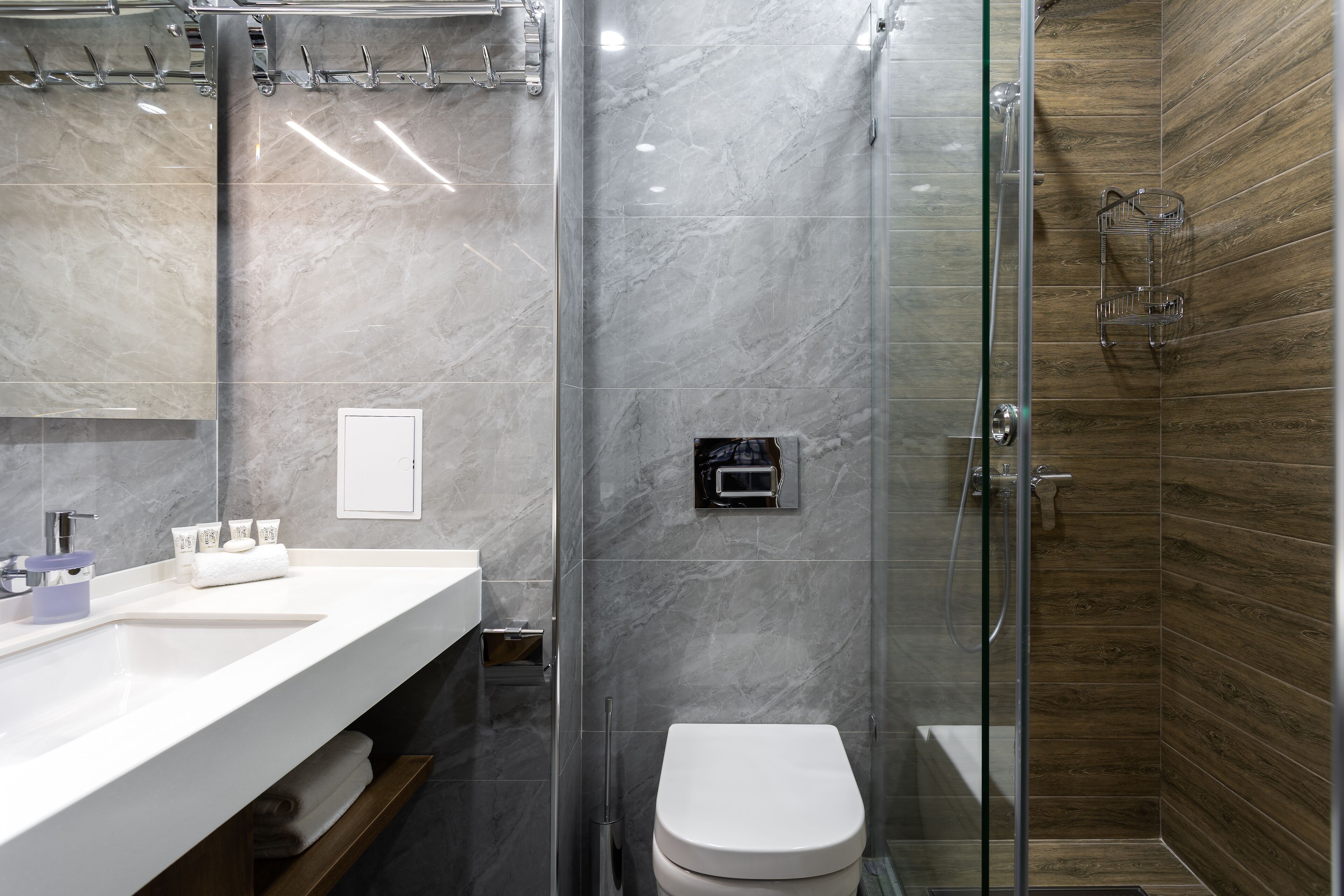 A modern bathroom with a marble vanity, a glass shower enclosure, and a wooden accent wall.