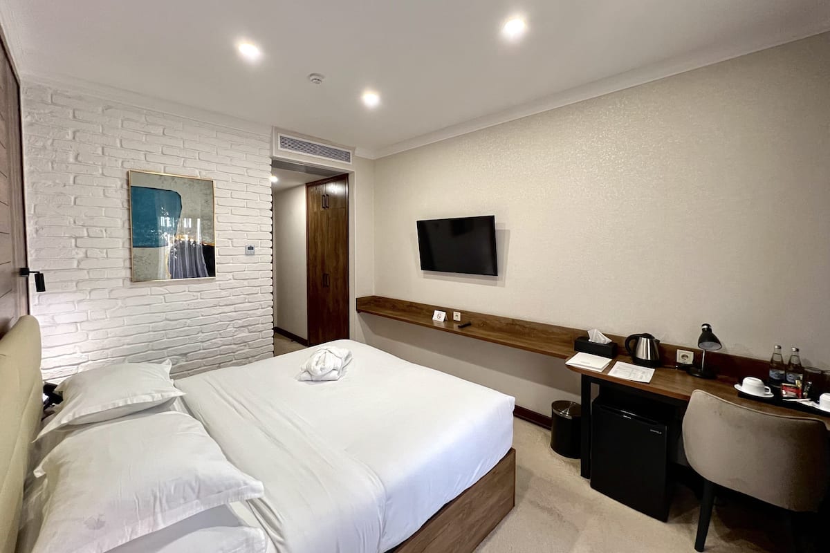 Una habitación de hotel con una cama, un escritorio, un televisor y un espejo.