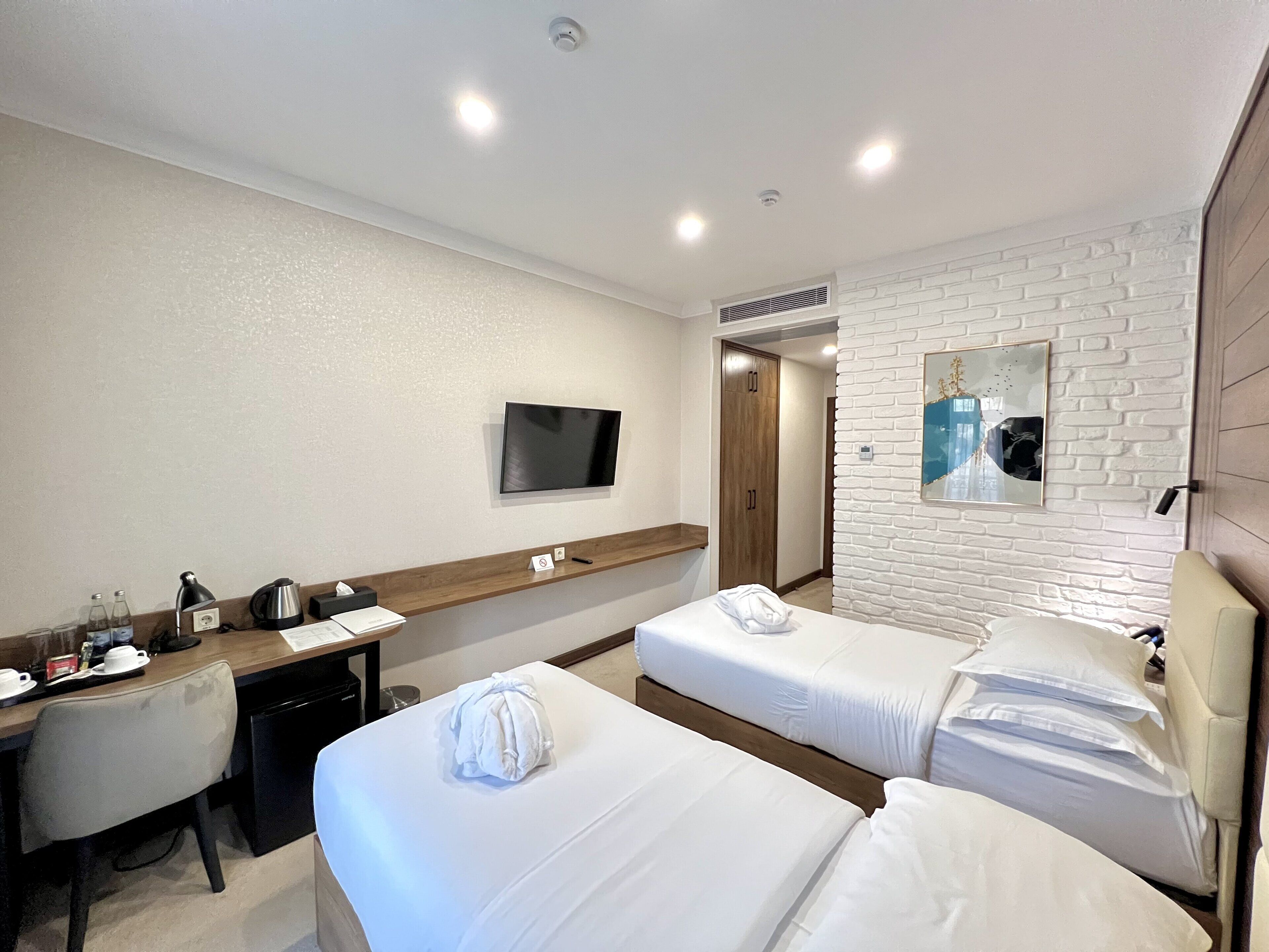 Een hotelkamer met twee bedden, een bureau met een computer, een televisie en een spiegel aan de muur.