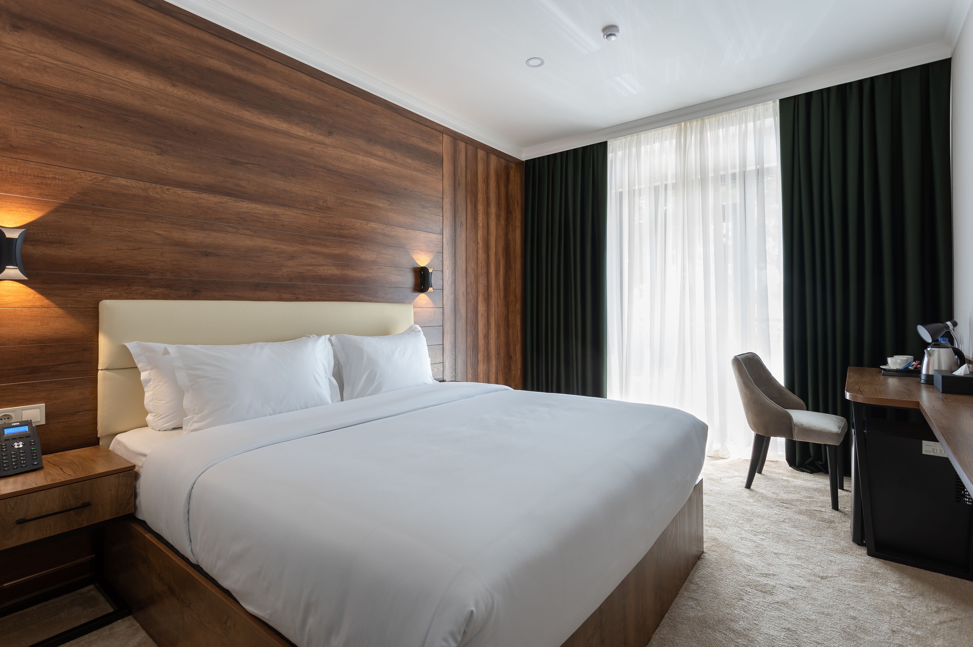 Een hotelkamer met een groot bed, een bureau, een stoel en een nachtkastje met een telefoon.