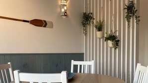 Un comedor con una mesa redonda de madera, sillas blancas tapizadas y una lámpara fijada a la pared.