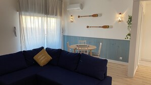 Una sala de estar con un sofá azul oscuro, una mesa redonda de madera y dos luces fijadas a la pared.