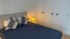 Un dormitorio con cama, almohadas, una mesita de noche, una lámpara y un armario.