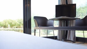 A modern hotel room with a large bed, a small table with a TV, and two chairs.