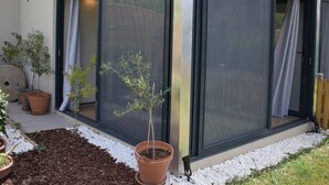 A modern building with large sliding glass doors, a small garden area with potted plants, and a tiled roof.