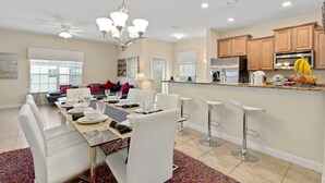 A modern kitchen with a central island, stainless steel appliances, and a dining area with white chairs and a glass table. - Disney 10mins, Free heated Private Pool, Security Gated, Luxury stay in Orlando (Kissimmee)
