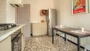A compact kitchen with a gas stove, a refrigerator, a wooden cabinet, and a dining table with chairs. - Appartamento con A/c, Lavastoviglie e Ascensore (Imperia)