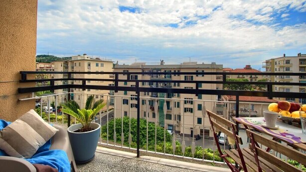 A balcony with a potted plant, a table with fruits, and a view of buildings. - Appartamento con A/c, Lavastoviglie e Ascensore (Imperia)