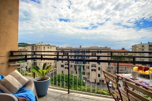 Ein Balkon mit einem Blumentopf, einem Tisch mit Früchten und Blick auf Gebäude.