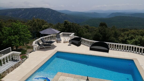 Una piscina con vista a las montañas, mobiliario exterior y una barandilla blanca.