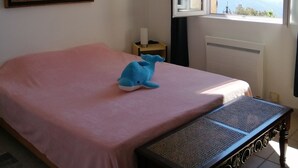 Un dormitorio con cama, una banca, un cuadro, una mesita de noche y una ventana con vistas.