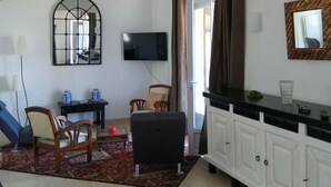 Una sala de estar con televisor, sofá, mesa de comedor y una zona de cocina con armarios.