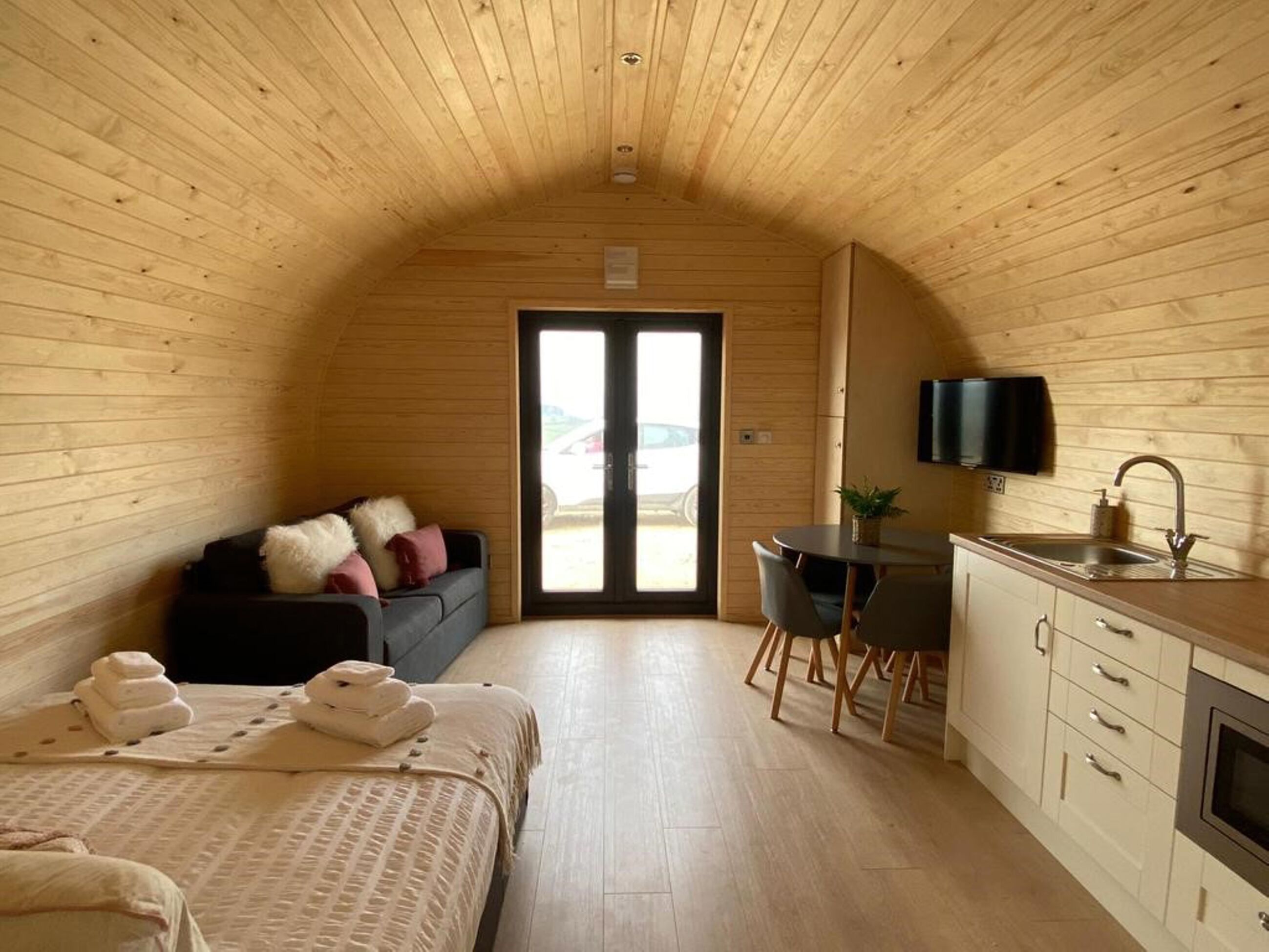 Une pièce chaleureuse aux murs lambrissés, comprenant un lit, un petit bureau, une chaise, un téléviseur et un lavabo.