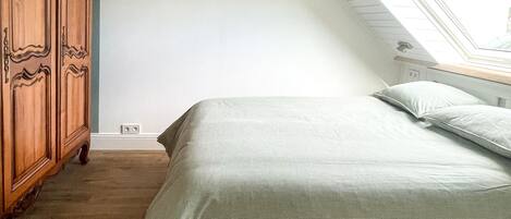 Een slaapkamer met een schuine kap, een dakraam, een houten garderobe en een bed met kussens.