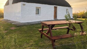 Un bâtiment blanc avec un toit noir, une porte en bois et une table de pique-nique devant.