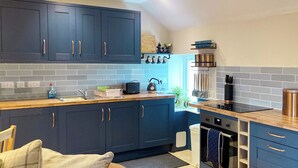 Une cuisine moderne avec des meubles de couleur bleu foncé, un plan de travail en bois et un four encastré.