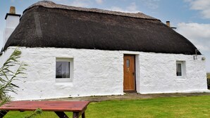 Une maison blanche avec un toit de chaume, une porte en bois et deux fenêtres.