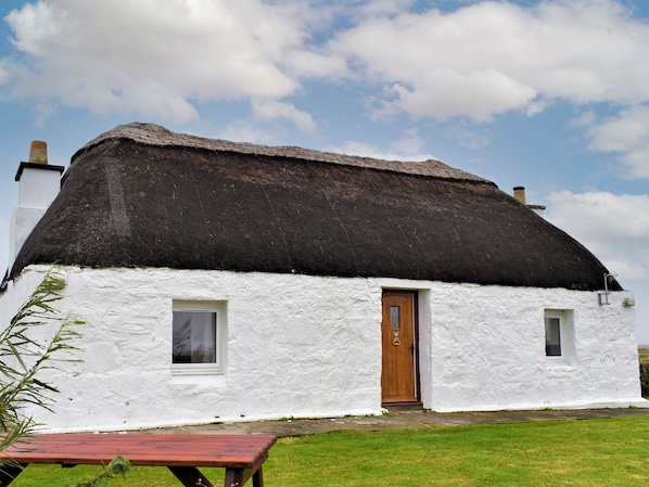 A white house with a thatched roof, a wooden door, and two windows.