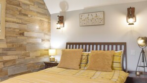 Une chambre à coucher avec une tête de lit en bois, un lit avec une literie jaune, une table de chevet avec une lampe et un luminaire fixé au mur.
