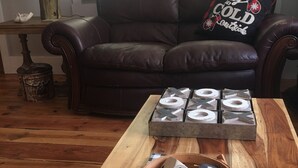 Een woonkamer met een bruine leren bank, een houten bijzettafeltje met dobbelstenen en een geweven mand.