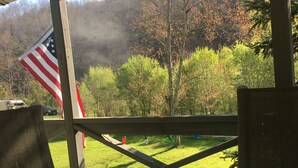Een overdekt buitengebied met een tafel, een vlag en uitzicht op een beboste heuvel.