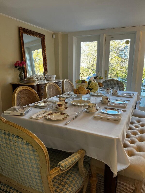 A dining room with a long table set for a meal, surrounded by chairs with patterned upholstery.