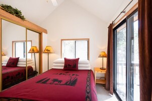 A bedroom with a large bed, two bedside lamps, a mirror, and a window with curtains.