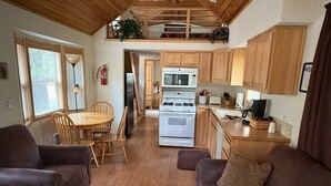 Un salon chaleureux avec une cheminée, un coin repas avec des meubles en bois, et une cuisine avec des armoires et des appareils électroménagers en bois.