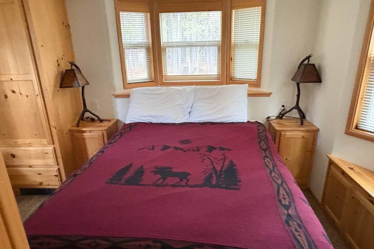 A bedroom with a bed, two nightstands, a window with blinds, and a wooden wardrobe.