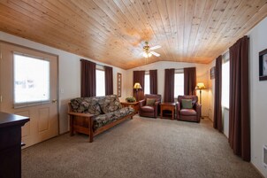 Una habitación acogedora con techo de madera, un sofá, dos sillones, una mesita y una lámpara de pie.