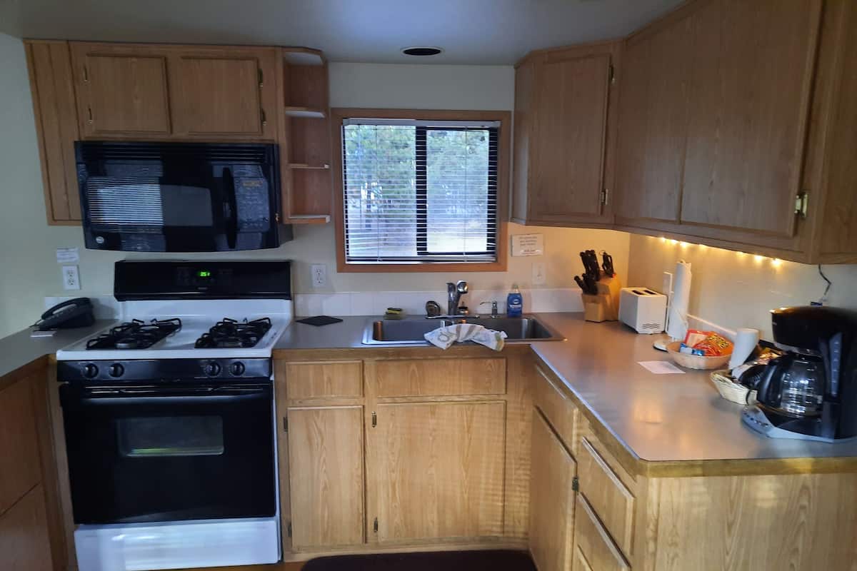 A compact kitchen with wooden cabinets, a microwave, stove, sink, and a coffee maker.