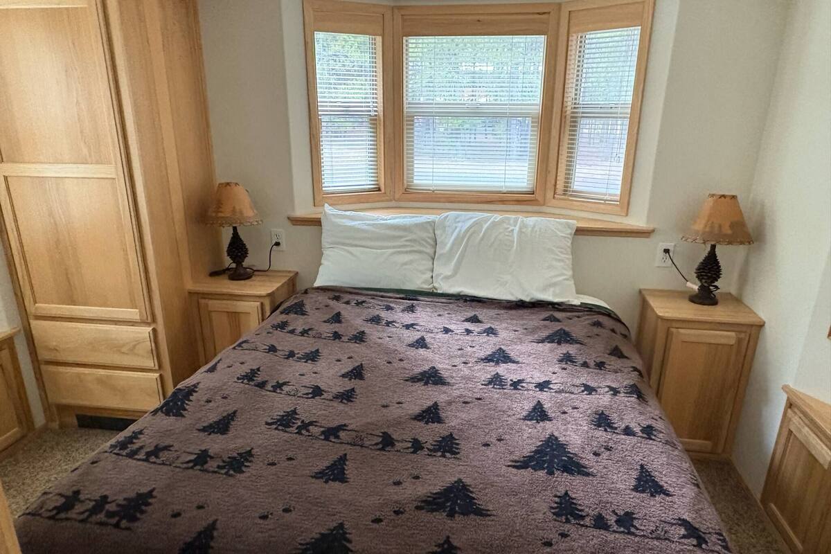 A bedroom with a bed, two nightstands, a window with blinds, and a wooden wardrobe.