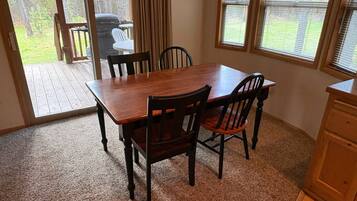 A dining area with a wooden table and four chairs, carpeted floor, and large windows with blinds.