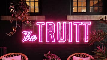 A neon sign reading "The TRUIT" with wicker chairs and potted plants.