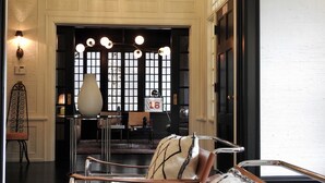 A room with a classic design, featuring a large window with a grid pattern, a chandelier, and a seating area with a patterned cushion. - Truitt Hotel (Kansas City)