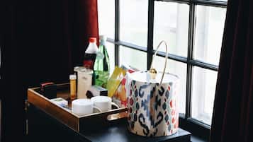 A tray with a patterned mug, a bottle, and some packaged snacks on a wooden table near a window with curtains.