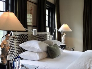 A hotel room with a neatly made bed, two bedside lamps, a decorative statue, and a window with curtains. - Truitt Hotel (Kansas City)