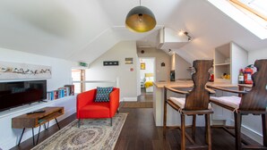 Una sala de estar moderna con un sofá rojo, una mesa de comedor de madera y sillas. Hay un televisor y una estantería con libros.