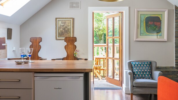 Una cocina con encimera de madera, lavavajillas integrado y comedor con una silla y una mesa.