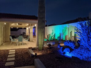 Relax outdoors with a dining table and comfortable seating, surrounded by a cactus and ambient lighting.