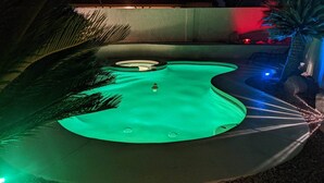 Une piscine dotée d’un espace de jacuzzi circulaire, entourée de palmiers et bordée de galets.