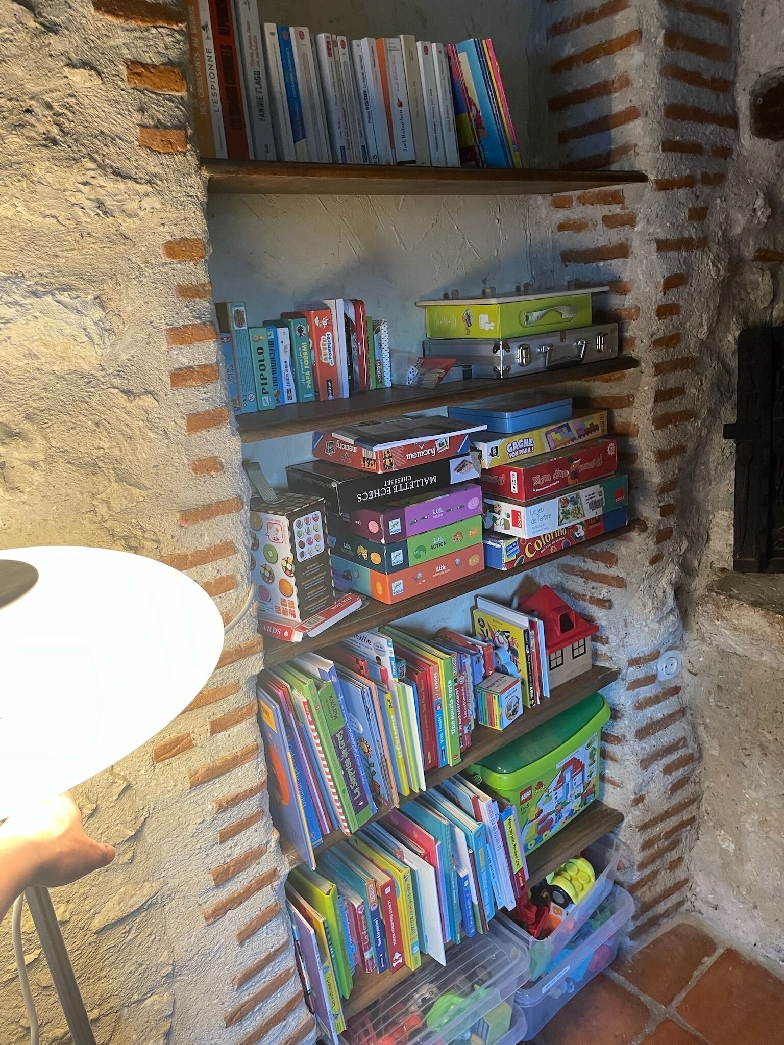 Une bibliothèque remplie de divers livres et jeux de société, adossée à un mur de briques.
