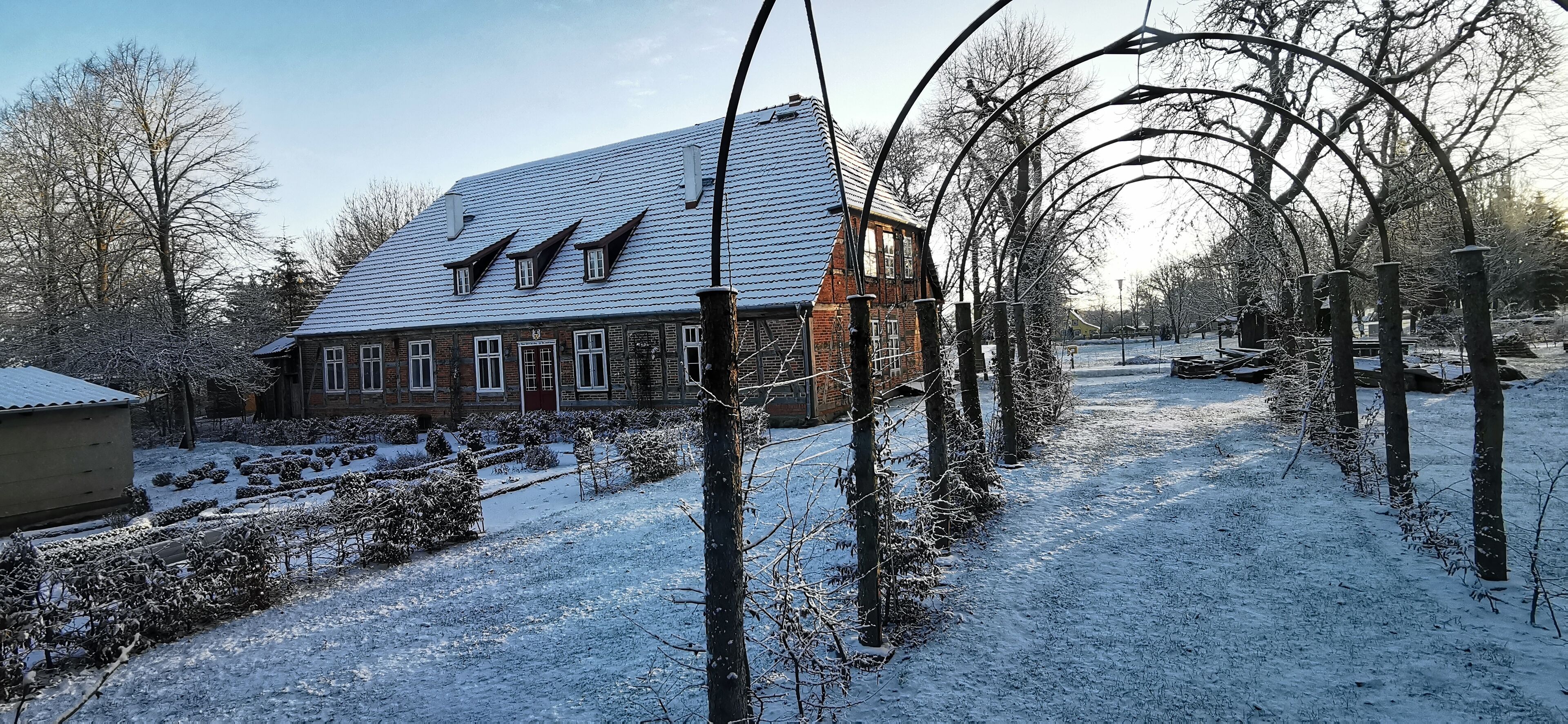 A snow-covered residential area with a brick house featuring a sloped roof and dormer windows.