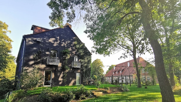 A large, rustic house with a steeply pitched roof, surrounded by lush greenery and trees. - Apartment Tilia (Ivenack)