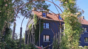 A two-story house with a red-tiled roof, surrounded by lush greenery and flowering plants. - Apartment Tilia (Ivenack)